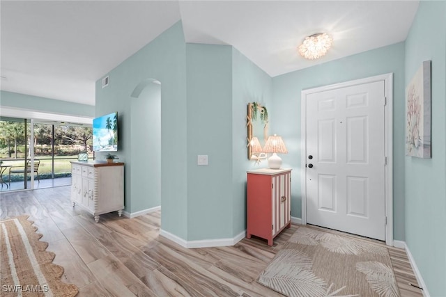 foyer entrance with light wood-type flooring, baseboards, visible vents, and arched walkways