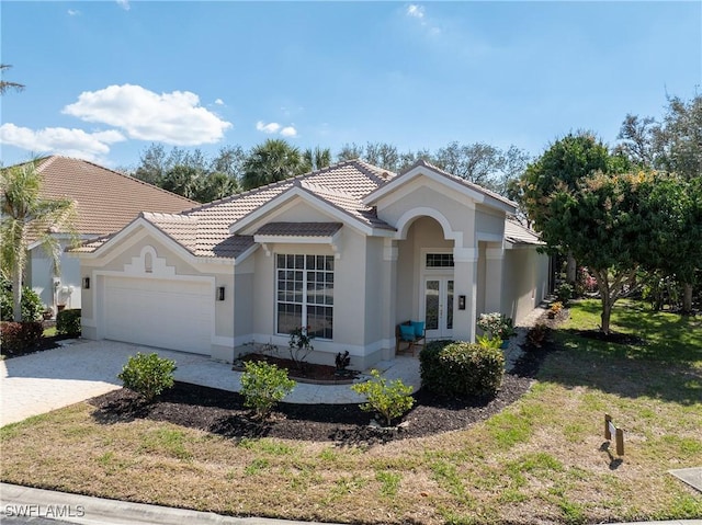 view of front of home with an attached garage, a tiled roof, french doors, decorative driveway, and stucco siding