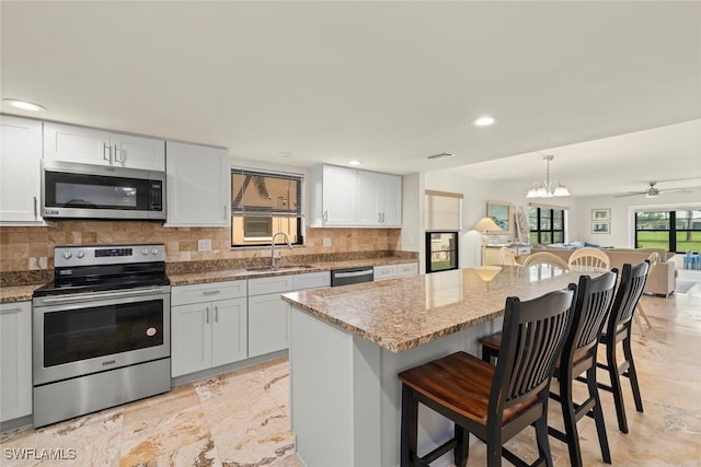 kitchen with a sink, a kitchen breakfast bar, appliances with stainless steel finishes, a center island, and decorative light fixtures