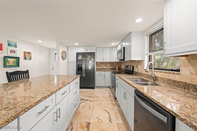 kitchen with white cabinets, light stone counters, stainless steel appliances, and a sink