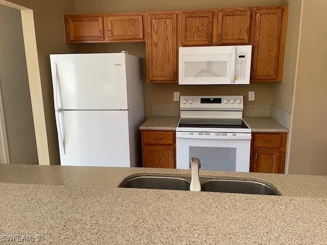 kitchen with white appliances, light stone counters, brown cabinetry, and a sink