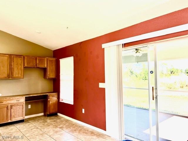 kitchen with lofted ceiling, light tile patterned floors, brown cabinetry, and built in study area