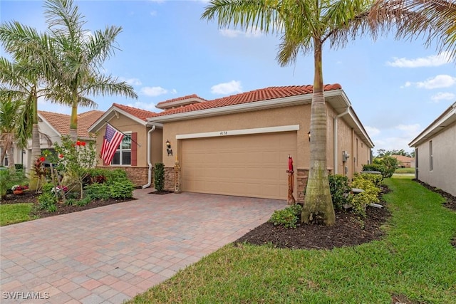 mediterranean / spanish-style home featuring decorative driveway, stucco siding, an attached garage, a front yard, and a tiled roof