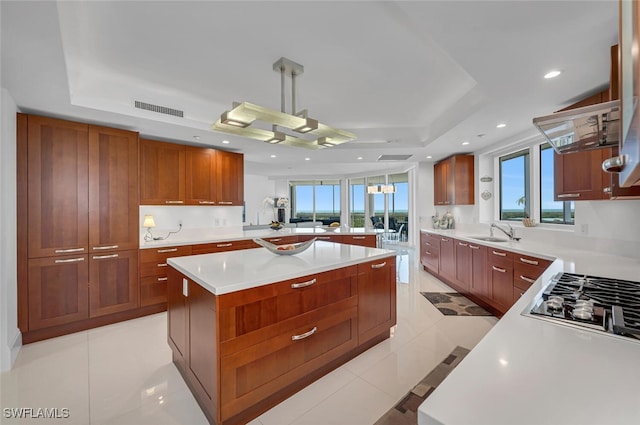 kitchen featuring a center island, a raised ceiling, light countertops, visible vents, and a sink