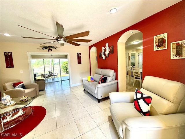 living room with arched walkways, light tile patterned floors, a ceiling fan, and baseboards