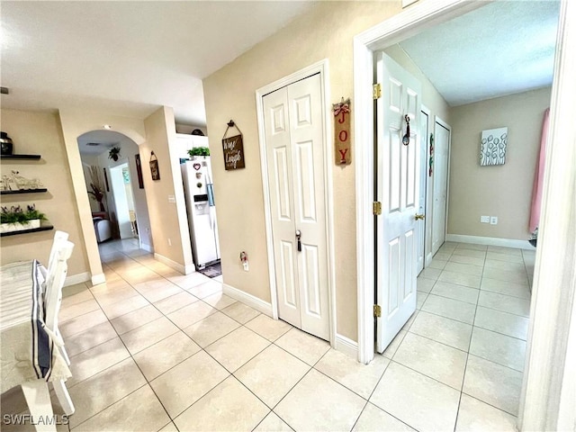 corridor with arched walkways, light tile patterned floors, and baseboards