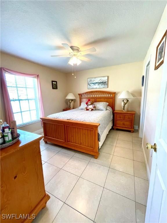 bedroom with a ceiling fan, a textured ceiling, baseboards, and light tile patterned floors