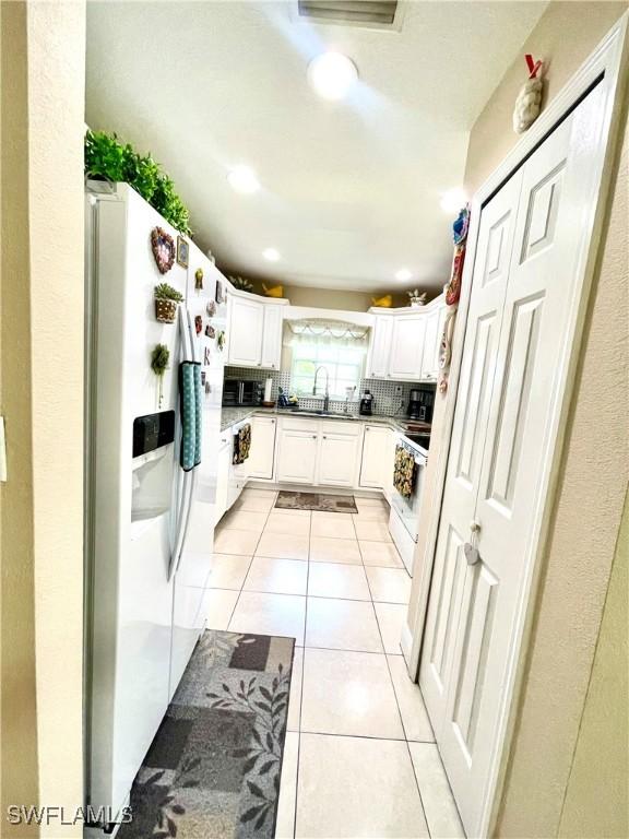 kitchen with white appliances, tasteful backsplash, light tile patterned floors, white cabinetry, and a sink