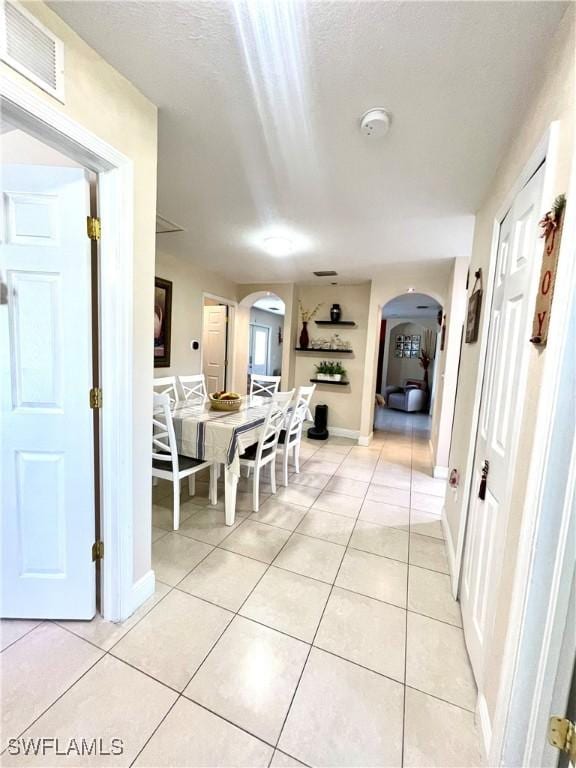 dining room featuring arched walkways, light tile patterned floors, visible vents, and baseboards