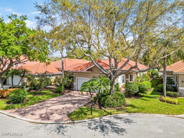 mediterranean / spanish-style home featuring an attached garage, a tile roof, decorative driveway, stucco siding, and a front yard