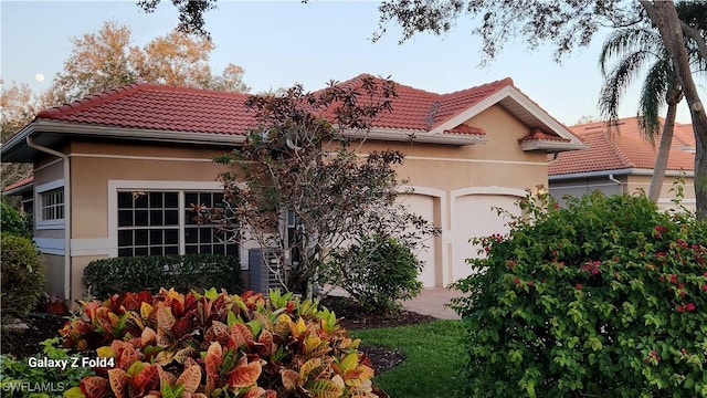 mediterranean / spanish home with an attached garage, driveway, a tile roof, and stucco siding