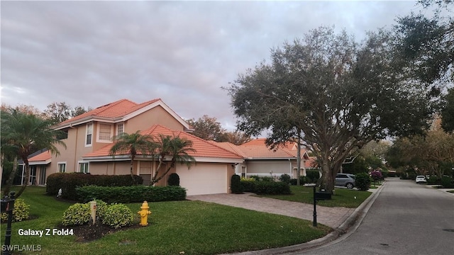 view of front of home with a garage, a tile roof, decorative driveway, a front lawn, and stucco siding