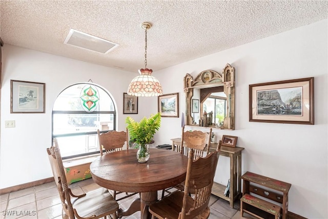 dining room featuring a textured ceiling, light tile patterned floors, attic access, and baseboards