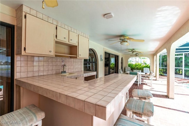 kitchen with tasteful backsplash, tile counters, a peninsula, cream cabinets, and a sink