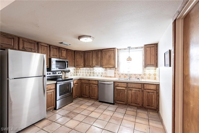 kitchen featuring visible vents, brown cabinetry, decorative backsplash, stainless steel appliances, and a sink