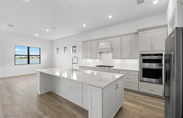 kitchen with wood finish floors, visible vents, appliances with stainless steel finishes, a sink, and premium range hood