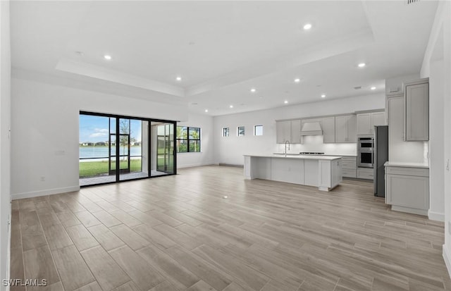 unfurnished living room featuring light wood-type flooring, a tray ceiling, and recessed lighting