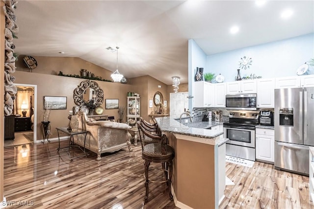 kitchen with a breakfast bar area, stainless steel appliances, a peninsula, white cabinetry, and light stone countertops