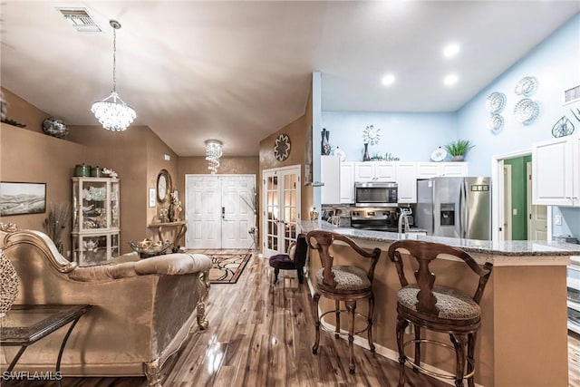 kitchen featuring visible vents, appliances with stainless steel finishes, a peninsula, light stone countertops, and white cabinetry