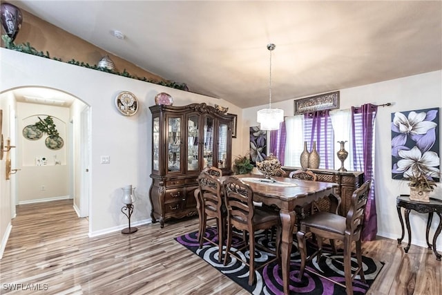 dining area with arched walkways, vaulted ceiling, baseboards, and light wood-style floors