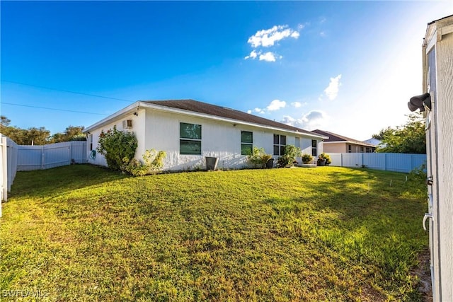 rear view of house featuring a fenced backyard, a lawn, and stucco siding