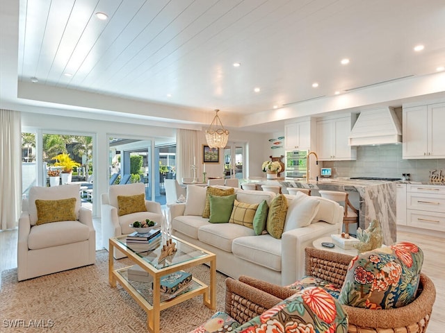 living room with light wood finished floors, a raised ceiling, a notable chandelier, and recessed lighting