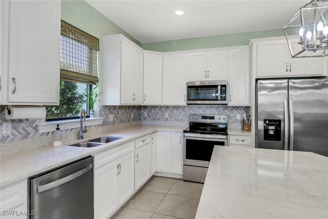 kitchen featuring white cabinets, light stone counters, stainless steel appliances, pendant lighting, and a sink