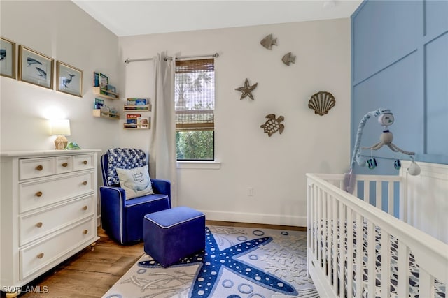 bedroom featuring a crib, baseboards, and wood finished floors