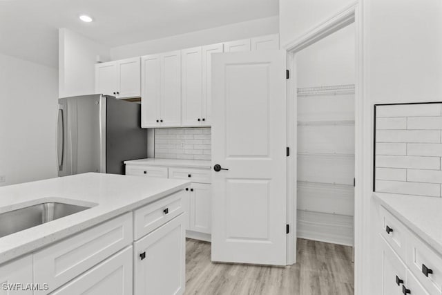 kitchen with light wood finished floors, decorative backsplash, freestanding refrigerator, and white cabinetry