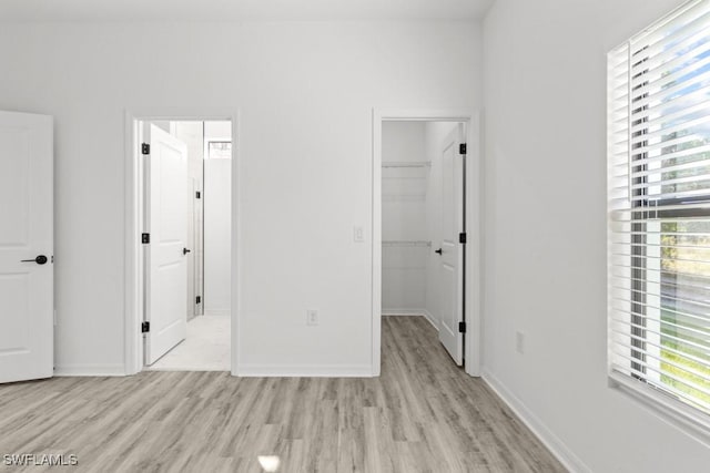 unfurnished bedroom featuring light wood finished floors, a closet, a walk in closet, and baseboards