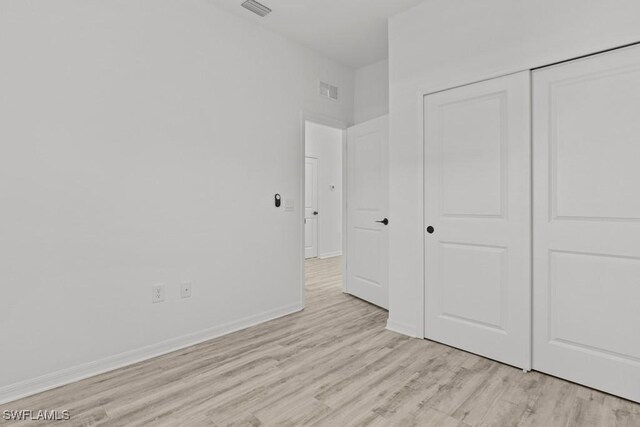 unfurnished bedroom with light wood-type flooring, a closet, visible vents, and baseboards