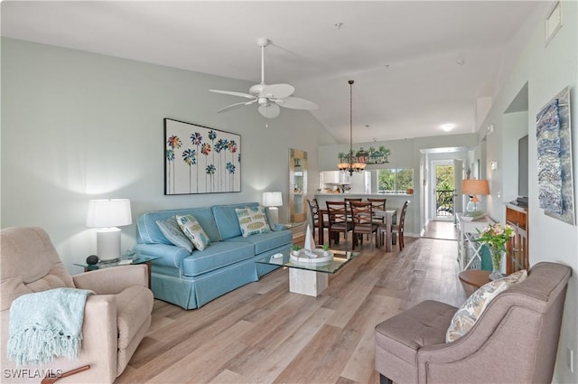 living room with lofted ceiling, light wood-style floors, and ceiling fan with notable chandelier