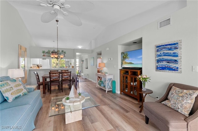 living room featuring visible vents, baseboards, lofted ceiling, light wood-style flooring, and ceiling fan with notable chandelier