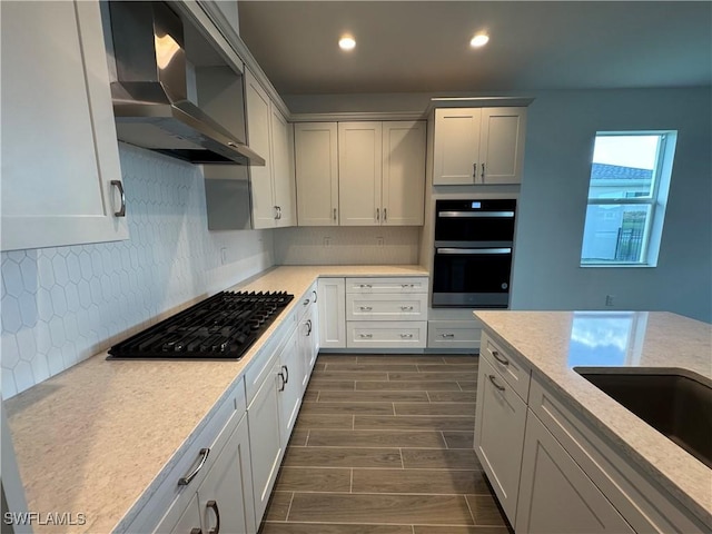 kitchen with tasteful backsplash, wall chimney exhaust hood, double wall oven, wood finish floors, and gas cooktop