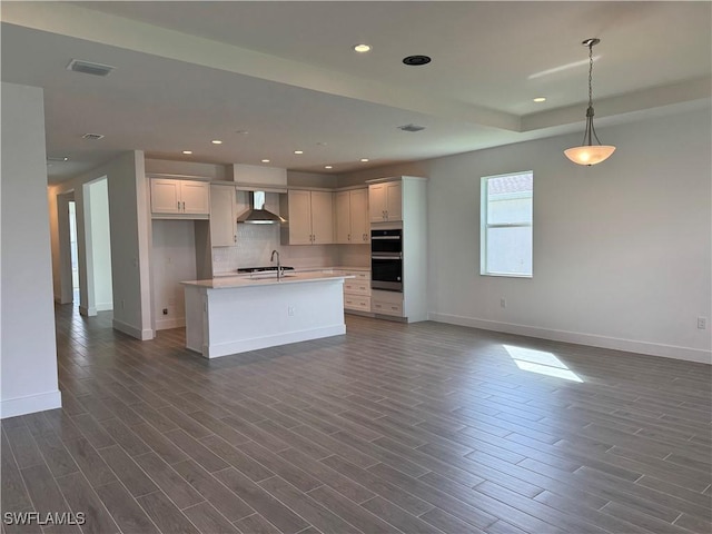 kitchen featuring dark wood-style flooring, light countertops, wall chimney range hood, and open floor plan