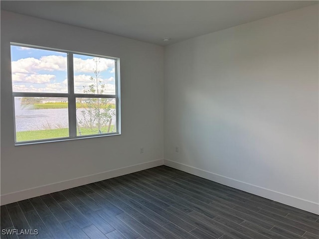 empty room with dark wood finished floors, baseboards, and a water view