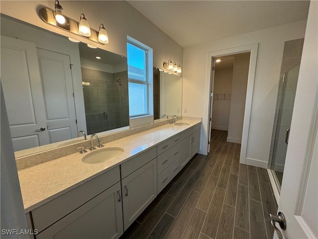 bathroom featuring a shower stall, double vanity, a sink, and wood tiled floor