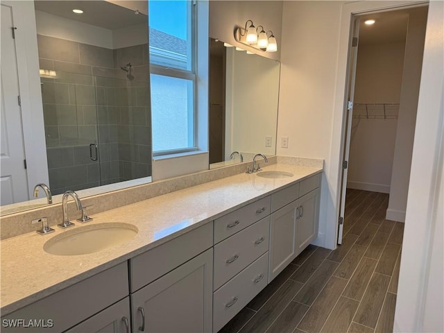 full bath featuring a shower stall, double vanity, a sink, and wood tiled floor