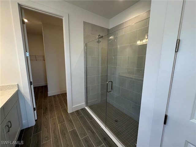 bathroom with baseboards, wood tiled floor, a walk in closet, vanity, and a shower stall