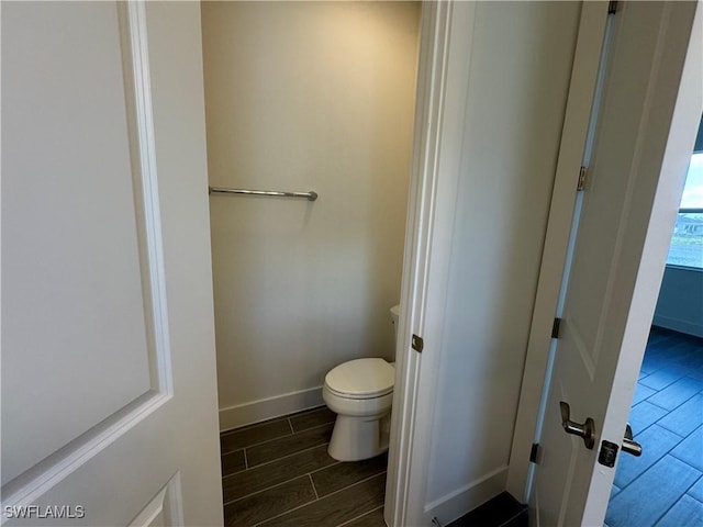 bathroom with wood finish floors, toilet, and baseboards