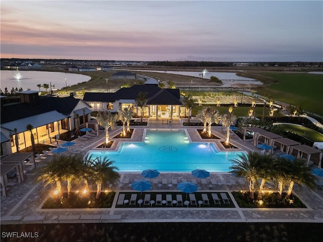 pool at dusk featuring a water view and a community pool