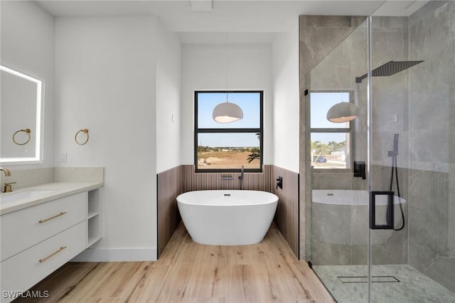 bathroom with a stall shower, a wainscoted wall, wood finished floors, vanity, and a freestanding tub