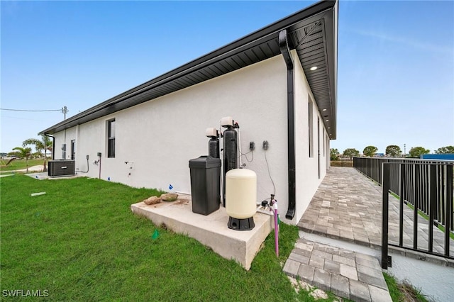 view of side of property with a patio, central air condition unit, fence, a lawn, and stucco siding