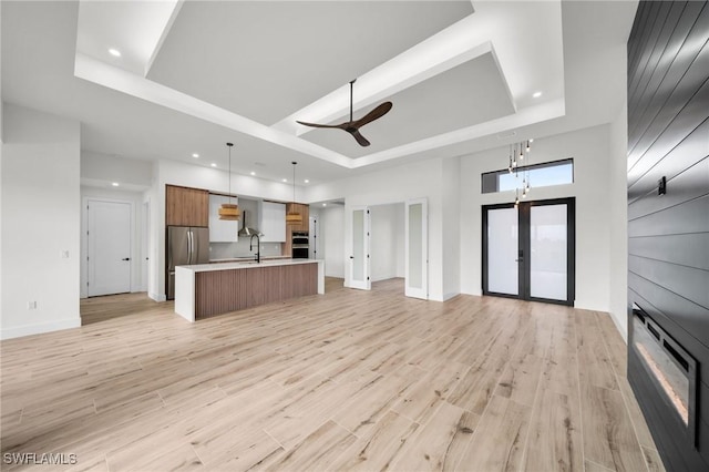 kitchen with a tray ceiling, light countertops, hanging light fixtures, open floor plan, and an island with sink