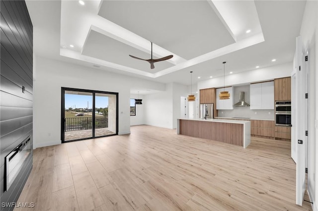 kitchen featuring a tray ceiling, light countertops, a large island, and wall chimney range hood