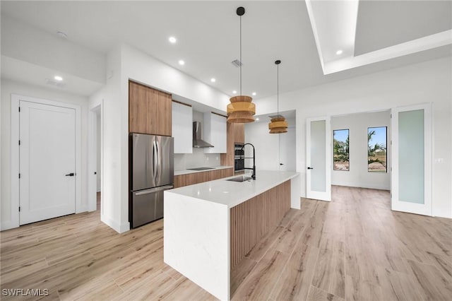 kitchen with a center island with sink, light countertops, hanging light fixtures, freestanding refrigerator, and a sink