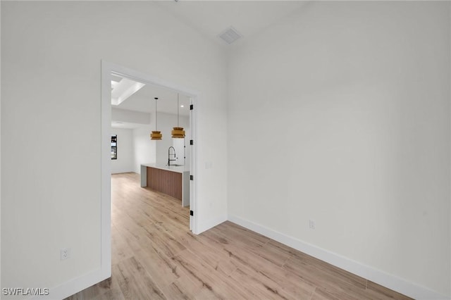 unfurnished room with light wood-type flooring, baseboards, visible vents, and a sink