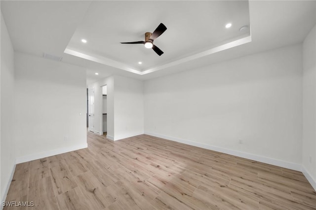 spare room featuring light wood finished floors, recessed lighting, a raised ceiling, and baseboards