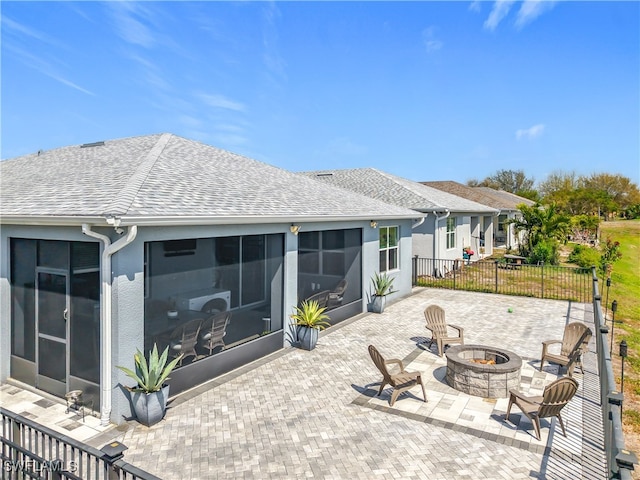 back of property with a shingled roof, an outdoor fire pit, a sunroom, fence, and a patio area