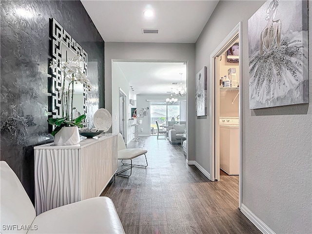 corridor featuring a textured wall, a notable chandelier, wood finished floors, visible vents, and baseboards